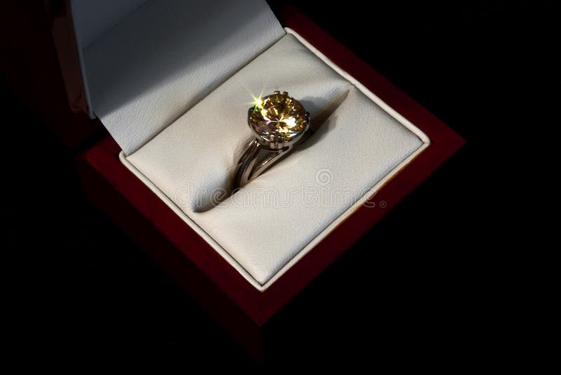 Finger ring with a yellow gemstone in a wooden gift box on black background