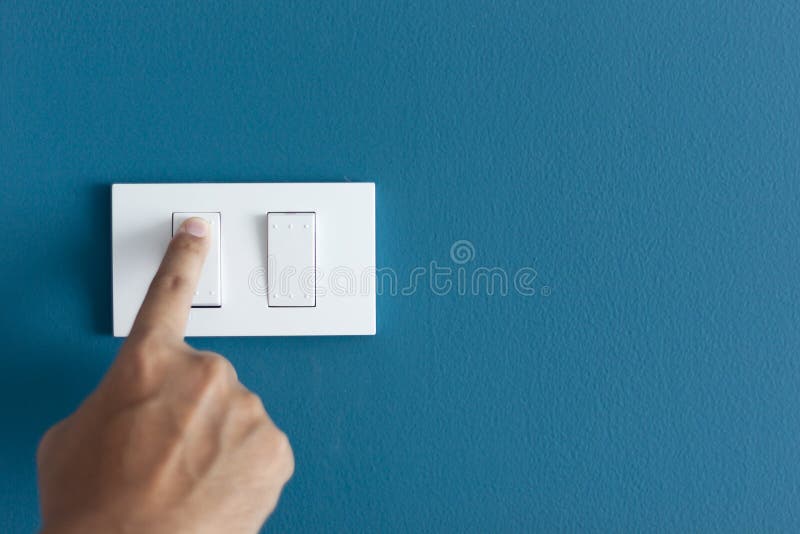 A finger turning on lighting switch on rough on blue dark wall. royalty free stock photography