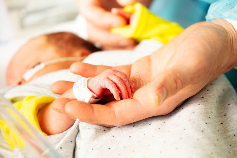 Close up of a mother`s hand and premature born infant child in ICU hospital room with monitor on. Close up of a mother`s hand and premature born infant child in ICU hospital room with monitor on