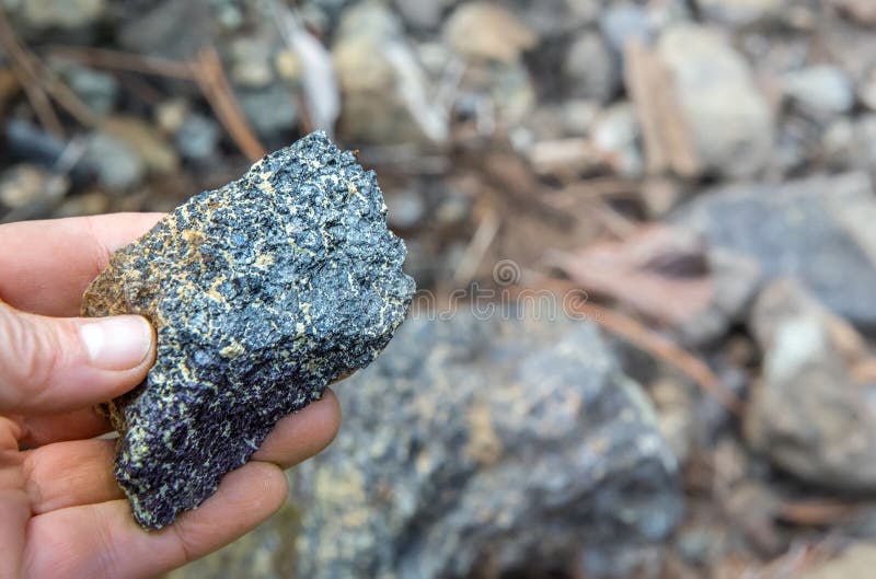 Fingers holding chromite ore over out of focus rocks background