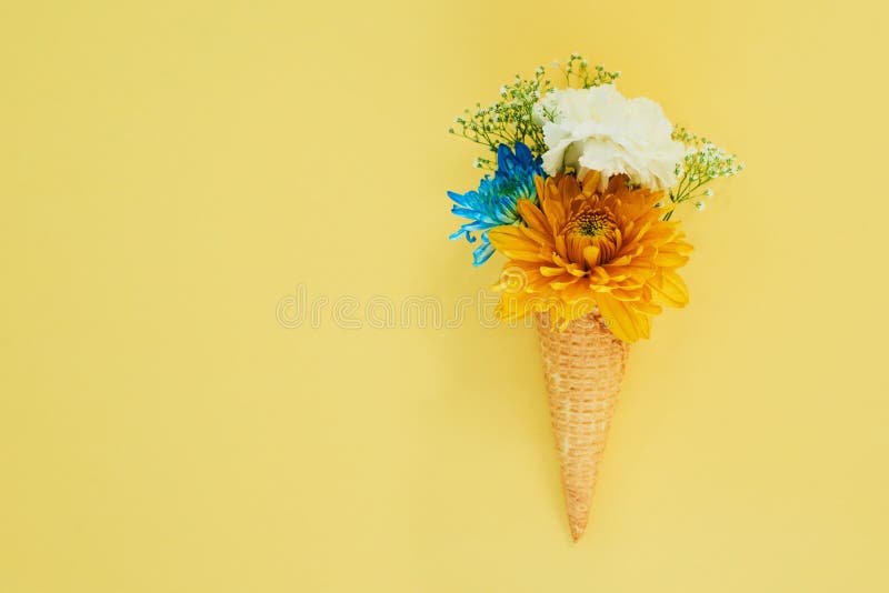 Fiori gelato in un cono in studio per l'arte o la decorazione creativa con bouquet fresco e colorato. creatività ancora. La creatività è ancora viva e le piante floreali in un dessert isolato da sfondo giallo con derisione.