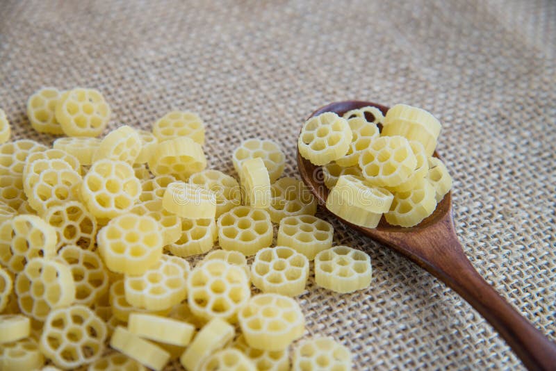 Fiori raw pasta in wooden spoon on sack rustic background . Natural and healthy food concept. Flower shape.