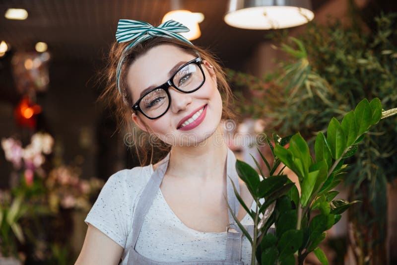 Fiorista grazioso allegro della giovane donna in vetri al negozio di fiore immagine stock libera da diritti Fiorista grazioso allegro della giovane donna in vetri al negozio di fiore immagine stock libera da diritti