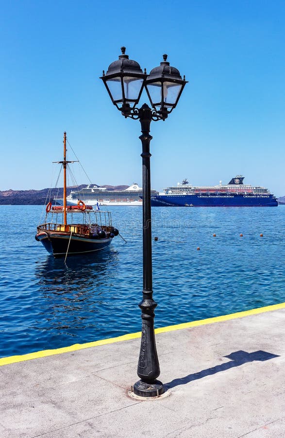 Fira, Santorini/Греция - 05-25-2014: 2 больших туристического судна и старой шлюпка в малой гавани Fira, Santorini, Греции стоковое фото rf Fira, Santorini/Греция - 05-25-2014: 2 больших туристического судна и старой шлюпка в малой гавани Fira, Santorini, Греции стоковое фото rf