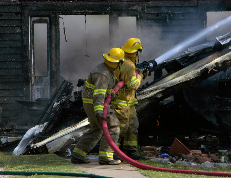 Una coppia di vigili del fuoco spruzzare acqua su un fumanti di rovine.