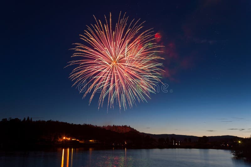 Celebration Fireworks Display Over a Mountain Lake at Dusk Stock Photo