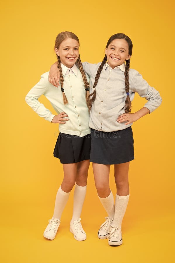 Firm friends. School girls with plaited hair in long braids. Cute little girls smiling on yellow background. Happy small