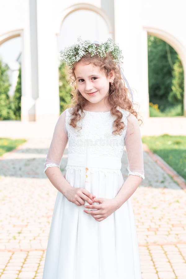 First communion girl. Portrait of cute little girl on white dress and wreath on first holy communion background church gate