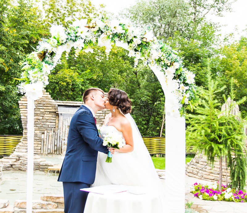 First Kiss of Newly Married Couple Under Wedding Arch Stock Photo