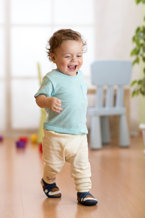 First steps of baby toddler learning to walk in living room. Footwear for little children.