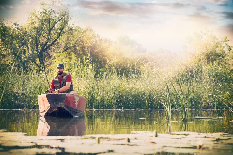 Fischer mit Angeln fischt in einem hölzernen Boot gegen Hintergrund der schönen Natur und des Sees oder des Flusses stockbild