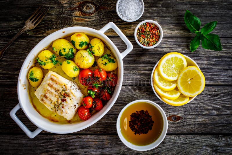 Fish dish - baked cod fillet with potatoes and cherry tomatoes on wooden table. Fish dish - baked cod fillet with potatoes and cherry tomatoes on wooden