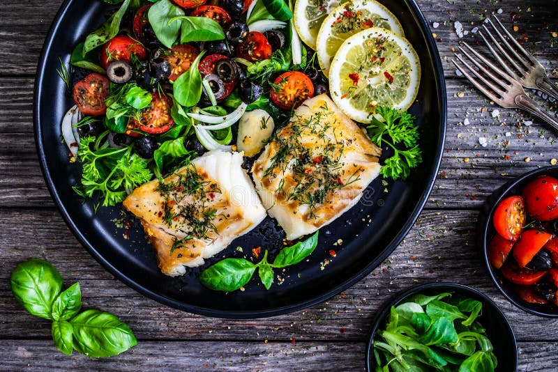 Fish dish - fried cod fillet with fresh vegetable salad on wooden table