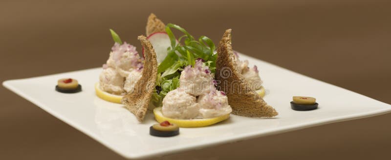 Fish roe salad,  whit toasted bread,  onion,  green leafs,  lemon,  radish and olives,  placed on a white plate,  brown background