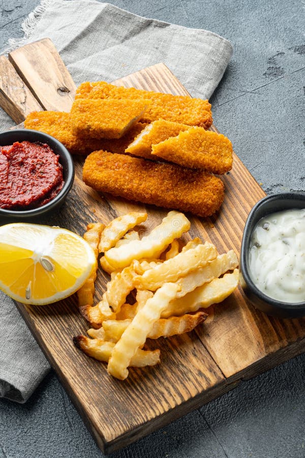 Fish Sticks with vegetables, on wooden cutting board, on gray background royalty free stock images