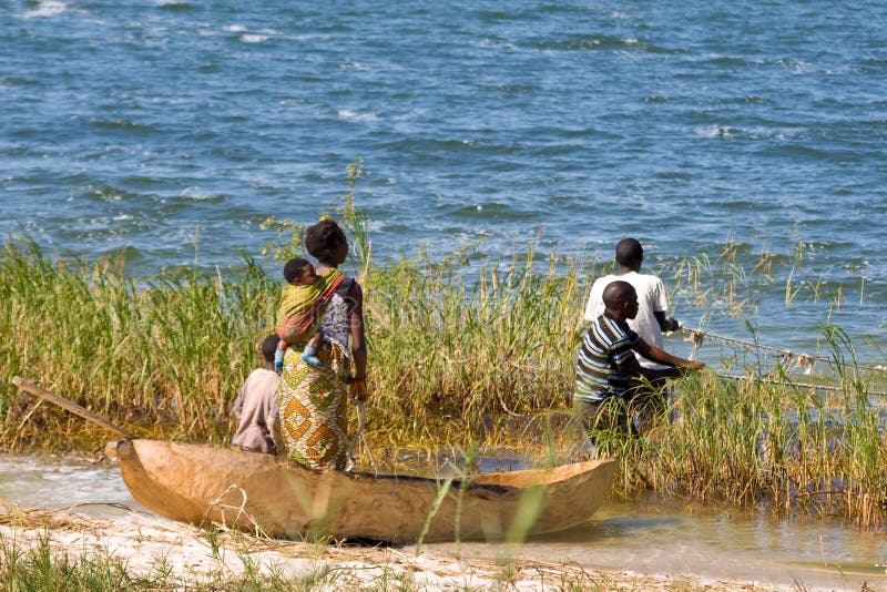 SAMFYA, ZAMBIA - JUNE 24, 2014: Two unidentified fisher men pull out the fishing net. One unidentified woman with her two unidentified kids stand in the fisher boat and wait for the catch at Lake Banguela. SAMFYA, ZAMBIA - JUNE 24, 2014: Two unidentified fisher men pull out the fishing net. One unidentified woman with her two unidentified kids stand in the fisher boat and wait for the catch at Lake Banguela.