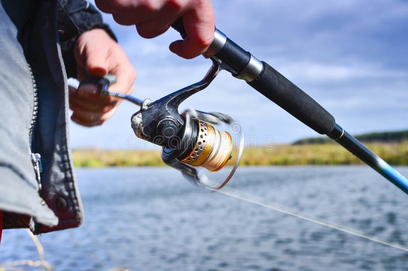 Premium Photo  Close up of spinning with the fishing reel in the hand  fishing hook on the line with the bait in the left hand against the  background of the water