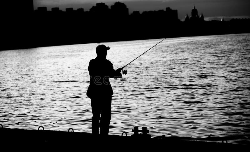 Fisherman standing on edge of dock with fishing rod near river in city