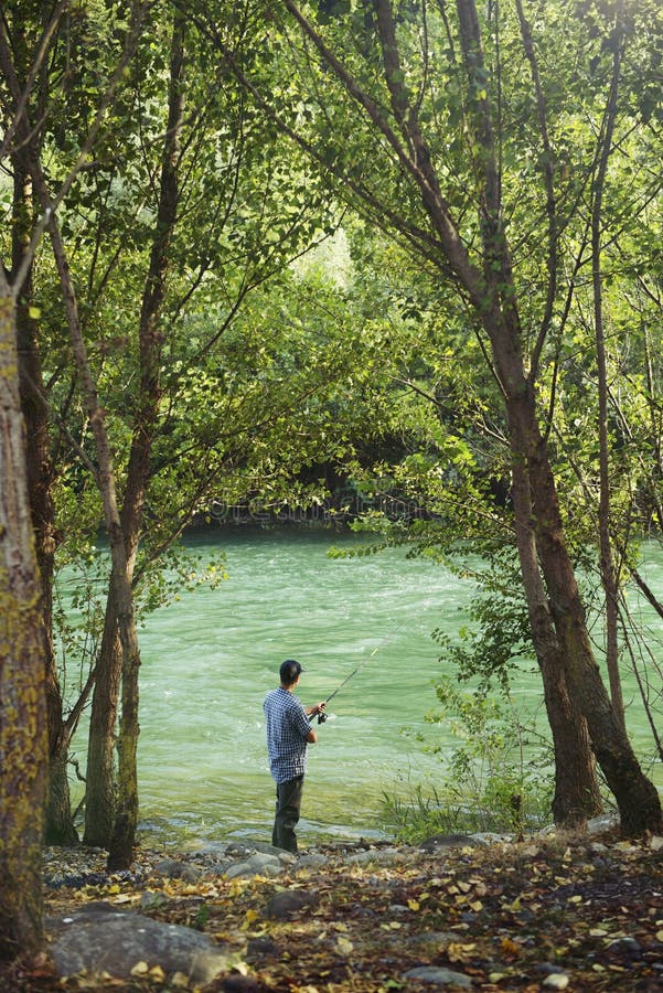 Fisherman standing near river and holding fishing rod