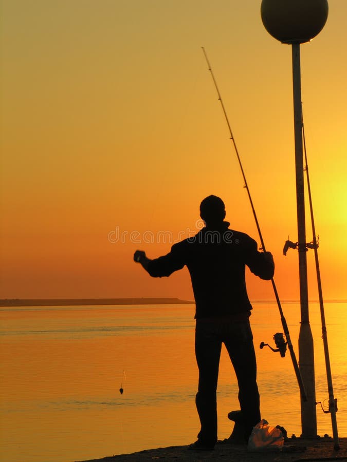 A fisherman standing by the sunset