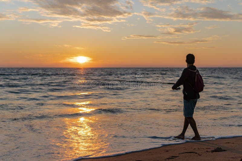 Fisherman stands on sandy beach during sunset