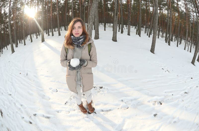 一件棕色外套的一个年轻和快乐的白种人女孩在一个积雪的森林里拿着一个雪球在冬天 Fisheye?? 免版税库存图片 一件棕色外套的一个年轻和快乐的白种人女孩在一个积雪的森林里拿着一个雪球在冬天 Fisheye?? 免版税库存图片
