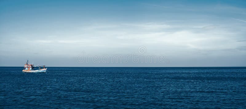 A fishing boat floats alone in the calm sea. The sky background above the horizon for copy space. Ocean nature landscape. The vessel is on the water. A fishing boat floats alone in the calm sea. The sky background above the horizon for copy space. Ocean nature landscape. The vessel is on the water