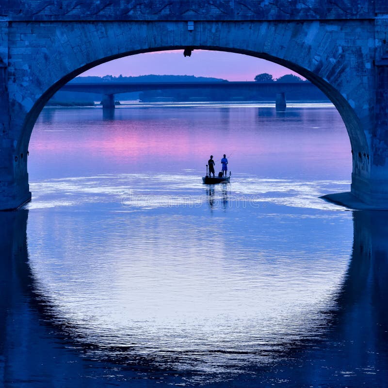 Fishing Boat Under the Arch of a Bridge in a Colorful Sunset Stock