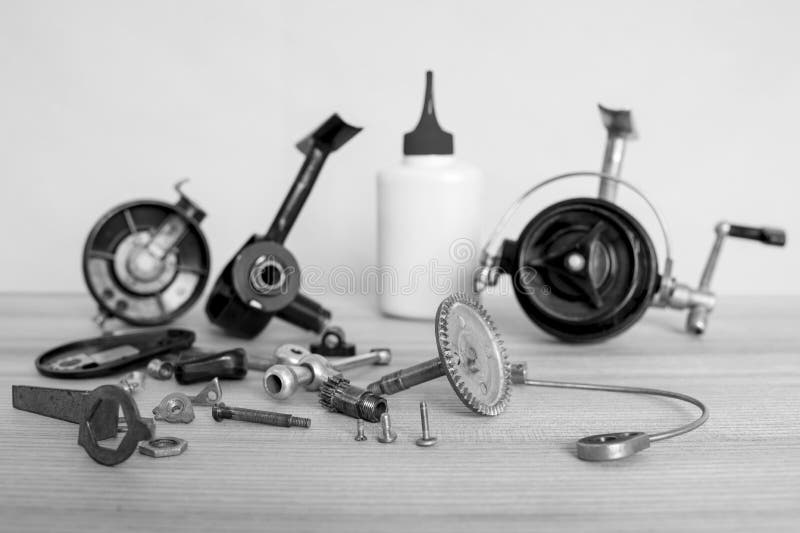 A fishing spinning reel as a whole and a second similar completely disassembled. Black and white image.