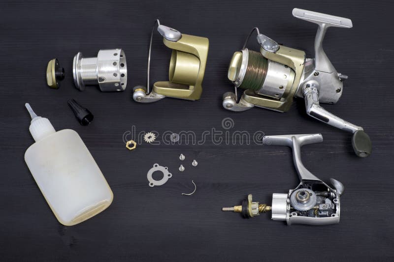 A fishing spinning reel as a whole and a second similar completely disassembled on a dark wooden background. Top view