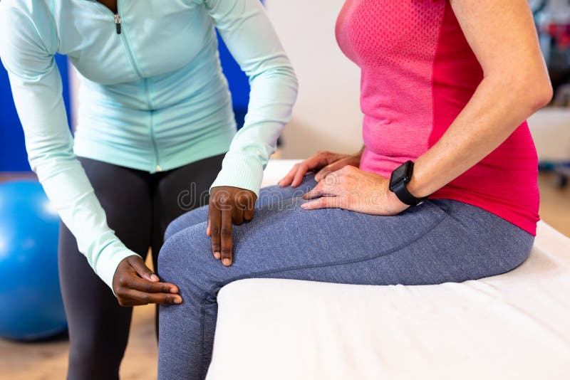Fisioterapeuta de sexo femenino que examina la pierna mayor activa de la mujer en centro de deportes fotos de archivo libres de regalías Fisioterapeuta de sexo femenino que examina la pierna mayor activa de la mujer en centro de deportes fotos de archivo libres de regalías