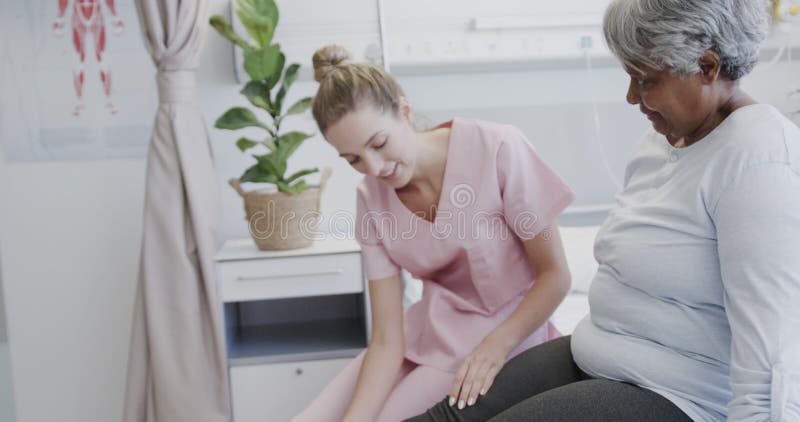 Fisioterapeuta femenina diversa feliz tratando la pierna de la paciente femenina de mayor edad a cámara lenta almacen de metraje de vídeo