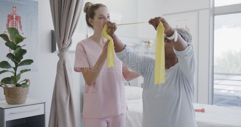 Fisioterapeuta femenina diversa feliz y paciente de edad avanzada que usa bandas de ejercicio a cámara lenta almacen de video