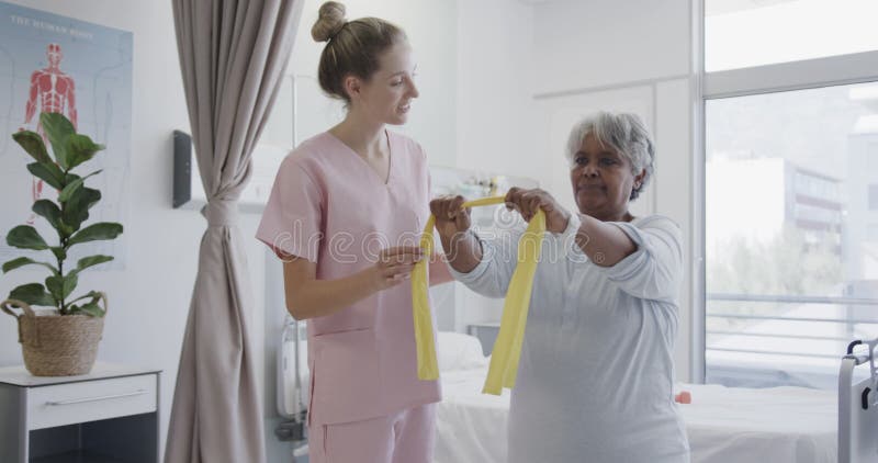 Fisioterapeuta femenina diversa feliz y paciente de edad avanzada que usa bandas de ejercicio a cámara lenta almacen de metraje de vídeo