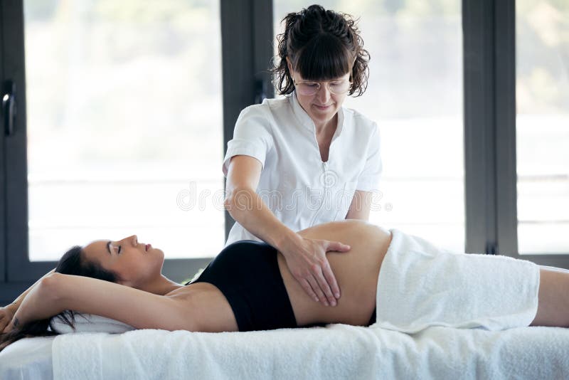 Fisioterapeuta fêmea que faz massagens a barriga na mulher gravida no centro dos termas fotografia de stock royalty free Fisioterapeuta fêmea que faz massagens a barriga na mulher gravida no centro dos termas fotografia de stock royalty free