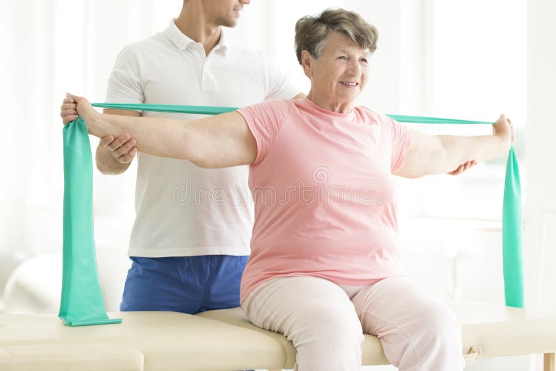 Physiotherapist providing help with easing the pain of joints through pnf exercises involving a scarf for his elderly patient. Physiotherapist providing help with easing the pain of joints through pnf exercises involving a scarf for his elderly patient