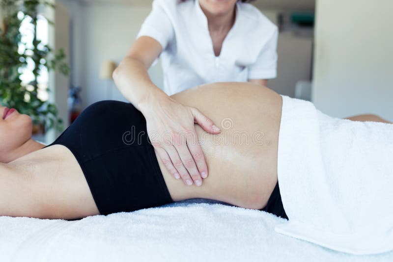 Fisioterapista femminile che massaggia pancia sulla donna incinta nel centro della stazione termale fotografia stock Fisioterapista femminile che massaggia pancia sulla donna incinta nel centro della stazione termale fotografia stock