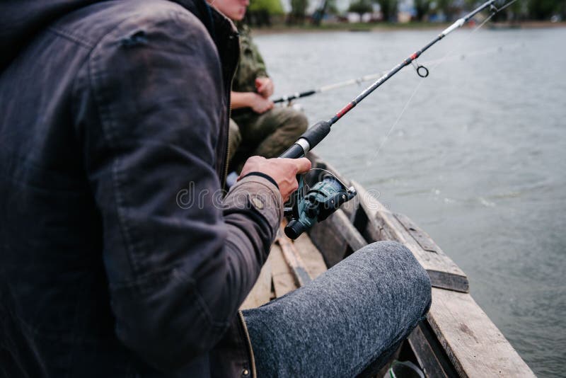 Fiskare f? ngar fisken att sitta i fartyget. Fiskare fångar fisken på floden, medan sitta i ett fartyg, vatten, himmel som är utomhus-, fiskaren, hobbyen, helgen, fiske, kopplar av, åtgärdar, beskådar, hakar, aktivt, manligt, rekreation, stången, lås, natur