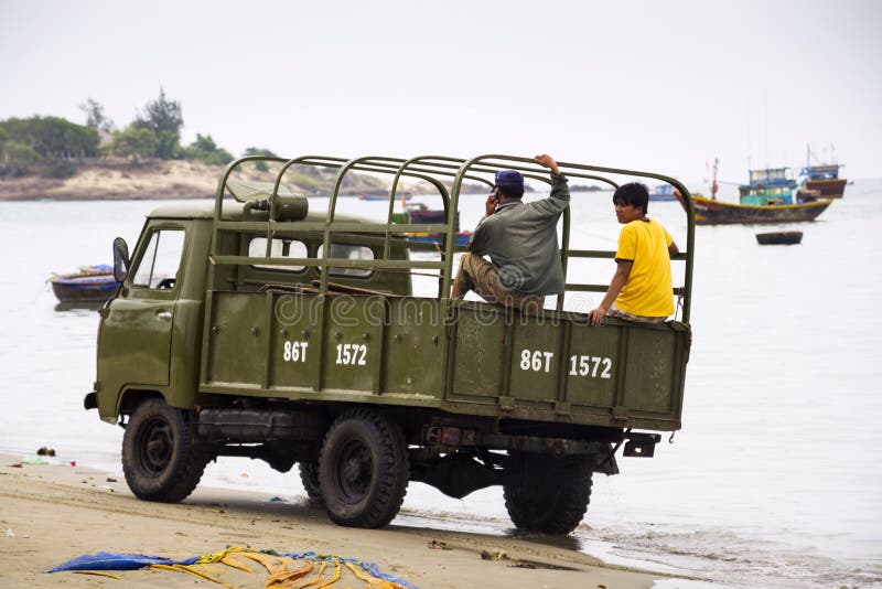 Fiskare som kör bilen på stranden med färgrika fiskebåtar på Februari 7, 2012 i Mui Ne, Vietnam royaltyfri foto Fiskare som kör bilen på stranden med färgrika fiskebåtar på Februari 7, 2012 i Mui Ne, Vietnam royaltyfri foto