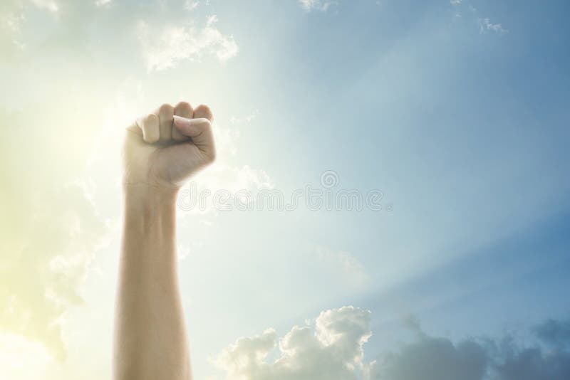 Fists of people raised in the air with clear sky and sunlight background.