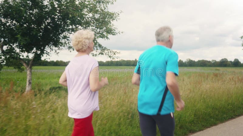Fit and active senior couple running outdoors as exercise. On path in summer