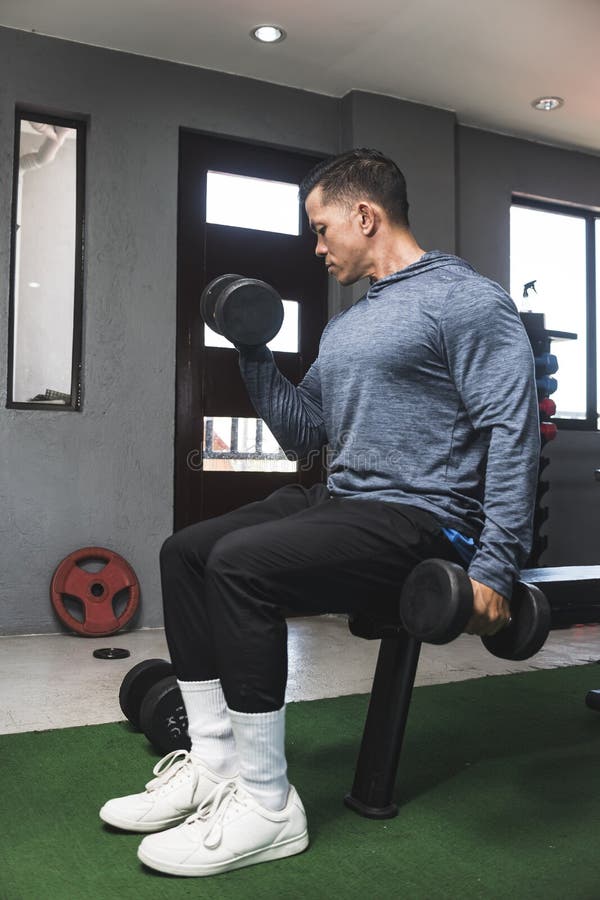 A Fit Athletic Asian Guy in a Sweatshirt Does Seated Alternate Dumbbell