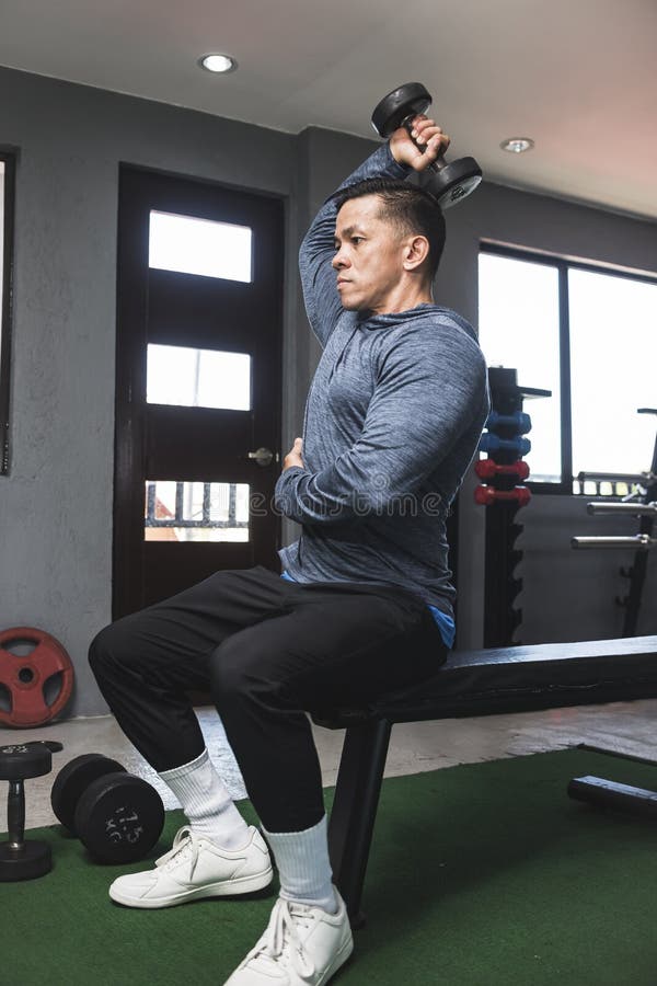 A Fit Athletic Asian Guy in a Sweatshirt Does Seated Overhead Dumbbell
