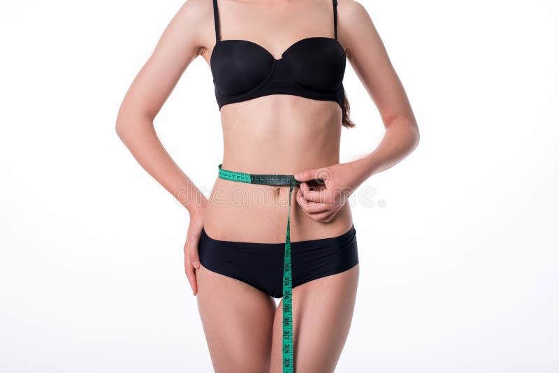 Fit and healthy young lady measuring her waist with a tape measure in centimeters and millimeters. She has her black gym