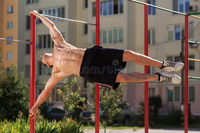 Fit man workout out arms on dips horizontal bars training triceps and biceps doing push ups outdoors.