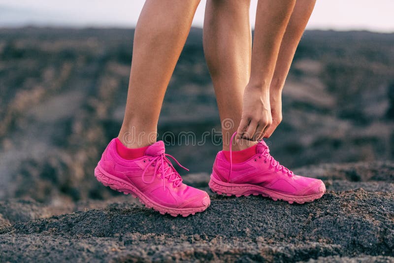 Fit run girl getting ready to walk on mountain rocsk tying up laces of trail running shoes - hot pink fashion footwear