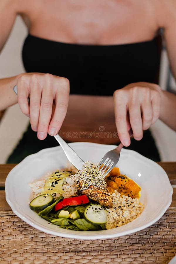 Fit woman in black top holding fork and knife eating vegan meal in a cafe close up.
