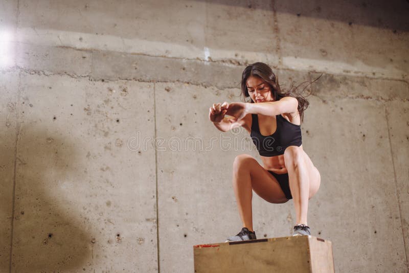 Fit woman doing a box jump exercise. Muscular woman doing a box squat at gym