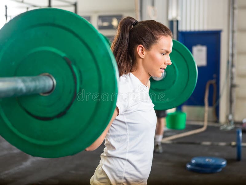 Side view of fit young woman lifting barbell in cross training box. Side view of fit young woman lifting barbell in cross training box