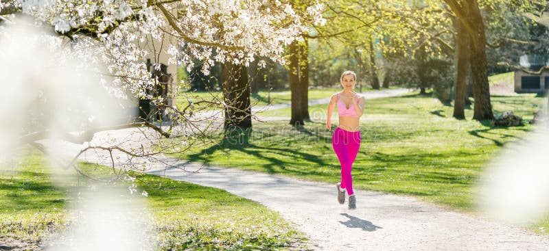 Fit woman running down a path during spring seen through blossom